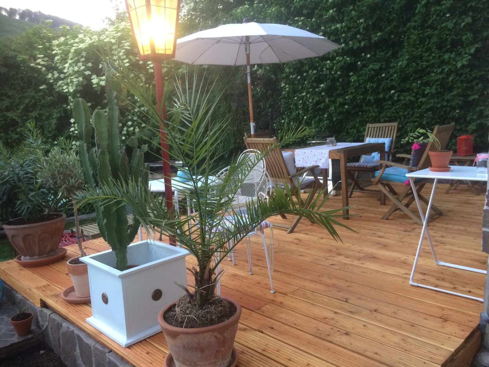 Sonnige Gartenterrasse des Hauses Feuchtl mit Holzdeck, Sonnenschirm und Pflanzen